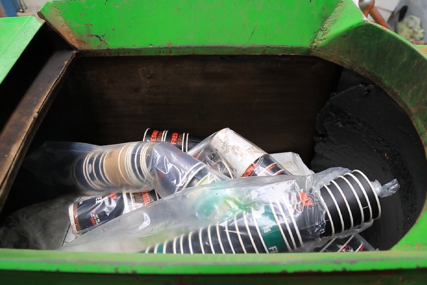 Coffee cups are seen in a green bin in tubes of plastic. There are around 50 of them.