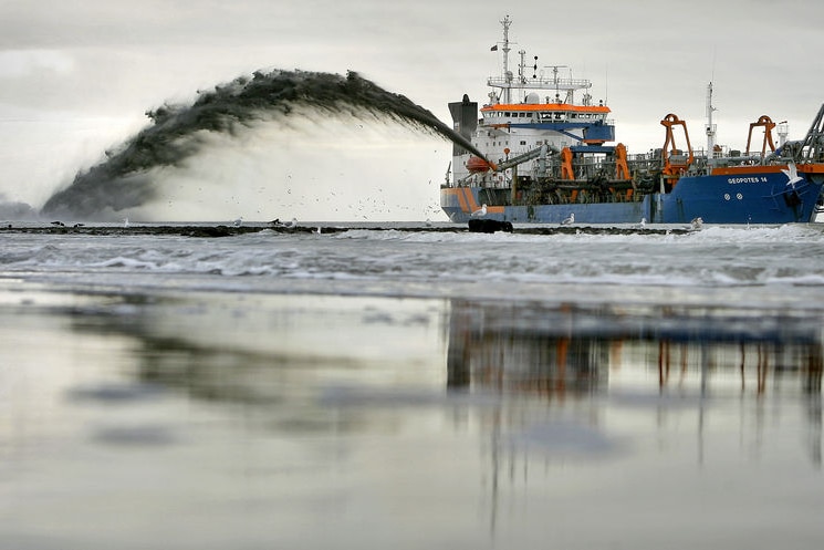 A big dredging boat sprays sand at the shore