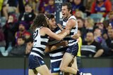 Three Geelong AFL players embrace as they celebrate a goal against the Brisbane Lions.