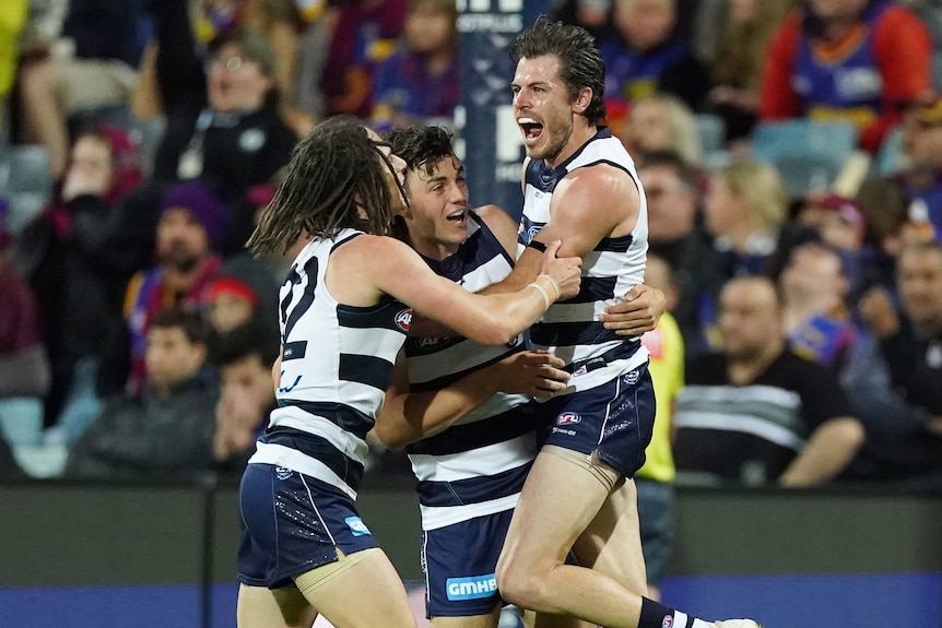 Three Geelong AFL players embrace as they celebrate a goal against the Brisbane Lions.