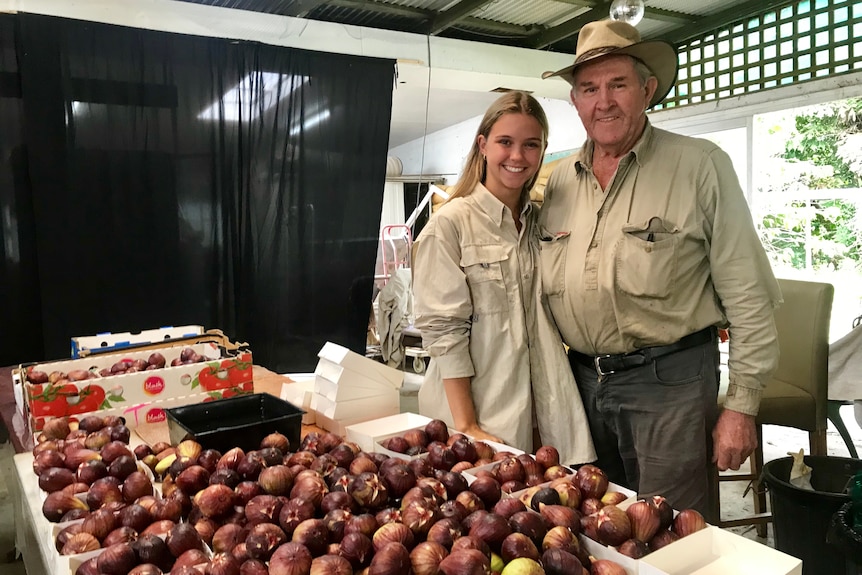 A man and  his granddaughter smile at the camera with figs covering a table