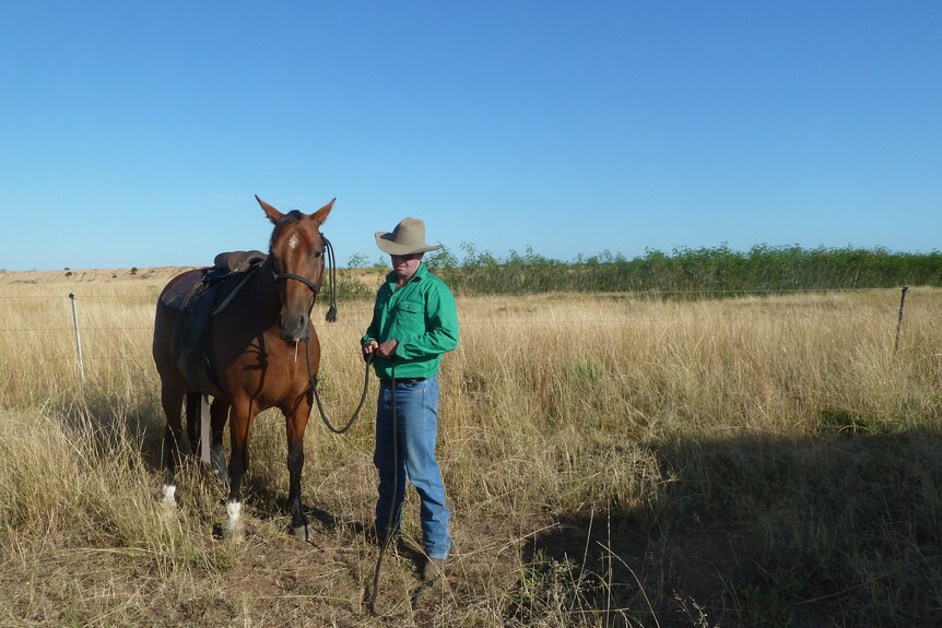 Detective Simon Jackson in a green shirt while beside is horse in a paddock  