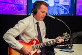 a man wearing  headphones playing a guitar inside a radio studio