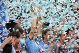 A soccer player wearing blue lifts a trophy as blue and white confetti flies through the air