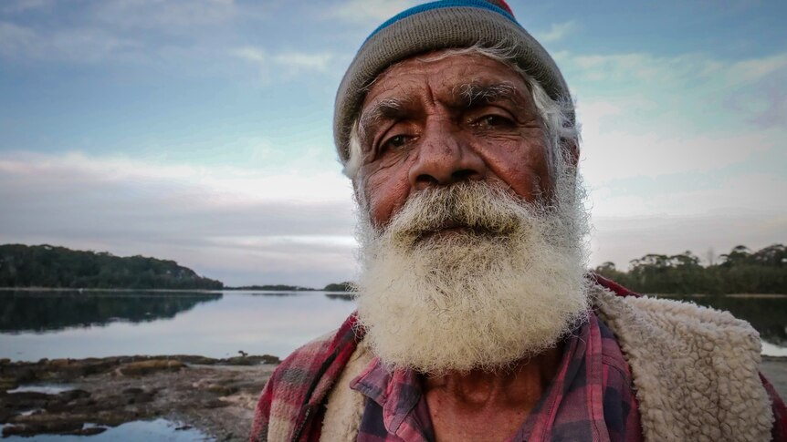 An older aboriginal man with a beanie on looking down the barrel of the camera  