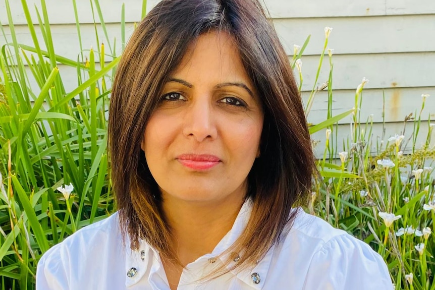 Dr Astha Tomar, a woman with short brown hair in a white shirt, poses for a photo in front of a weatherboard building