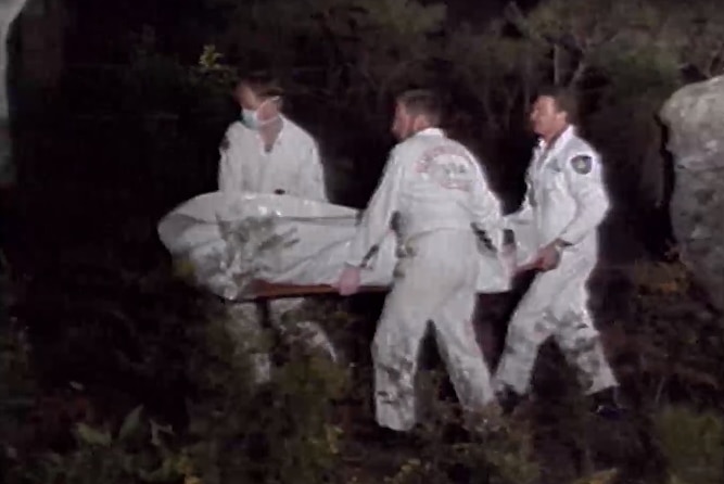 Four people holding a stretcher with a body on it wrapped in plastic