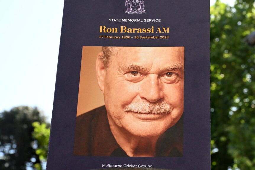 An order-of-service for the Ron Barassi memorial service, beside his bronze statue at the MCG.