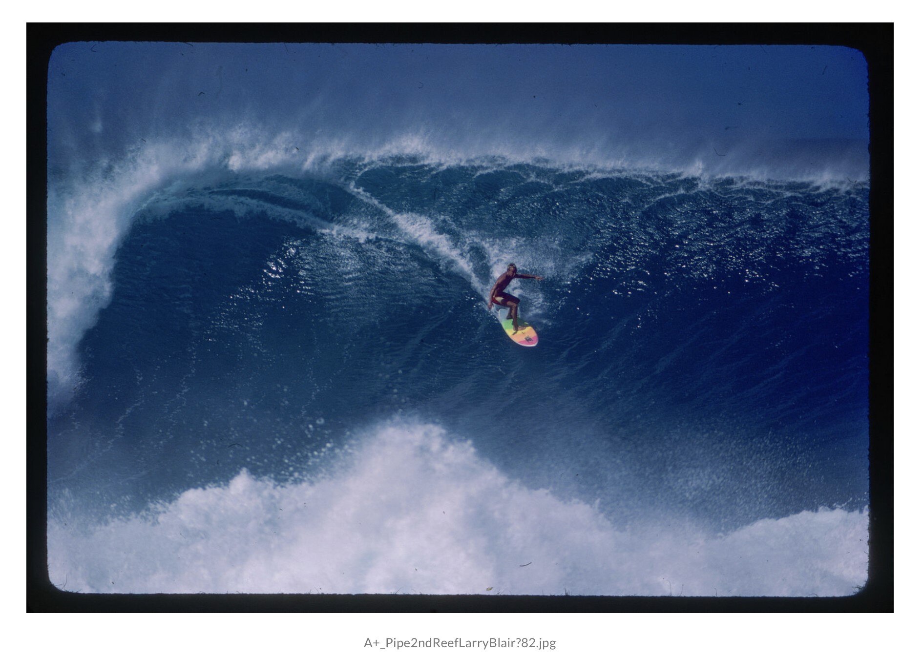 An old coloured photo of a man surfing a giant wave on a garrish board.