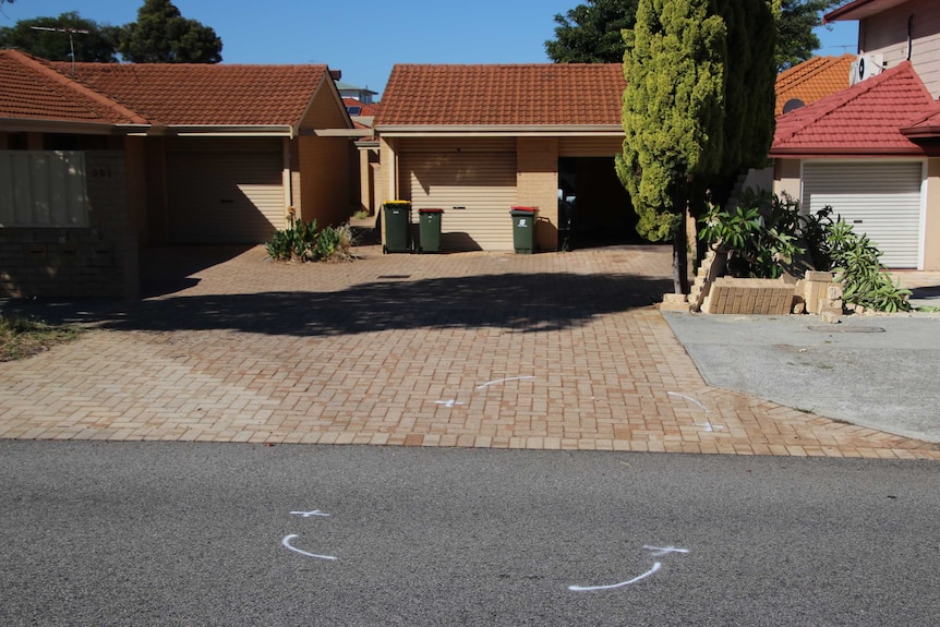 A driveway to a block of houses with three garage doors and a road in front with white outlines of a car.