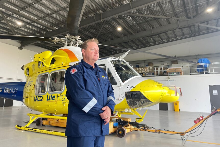 Man in uniform stands beside helicopter