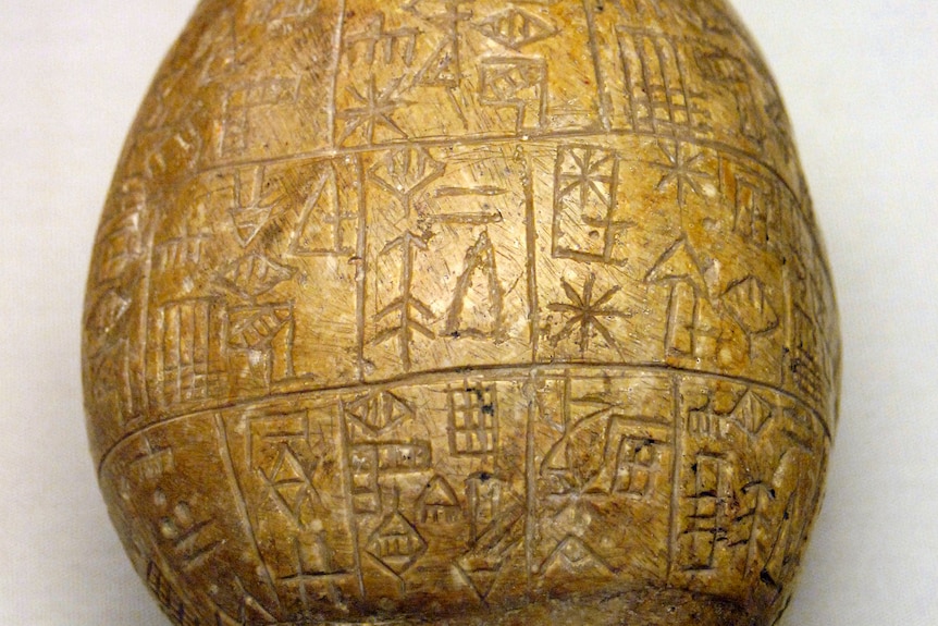 Close-up of a square piece of pale rock with a series of lines, circles and other shapes and symbols inscribed in it.