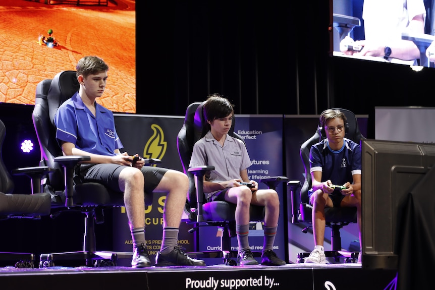 three students in their school uniform on stage playing mario kart