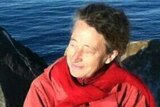 Monika Billen wears a red jacket and sits by the ocean