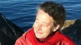 Monika Billen wears a red jacket and sits by the ocean