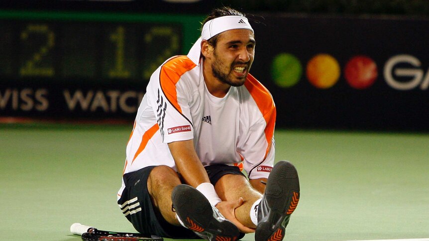 Marcos Baghdatis grimaces and holds his calf while sitting on the court during the Australian Open final.