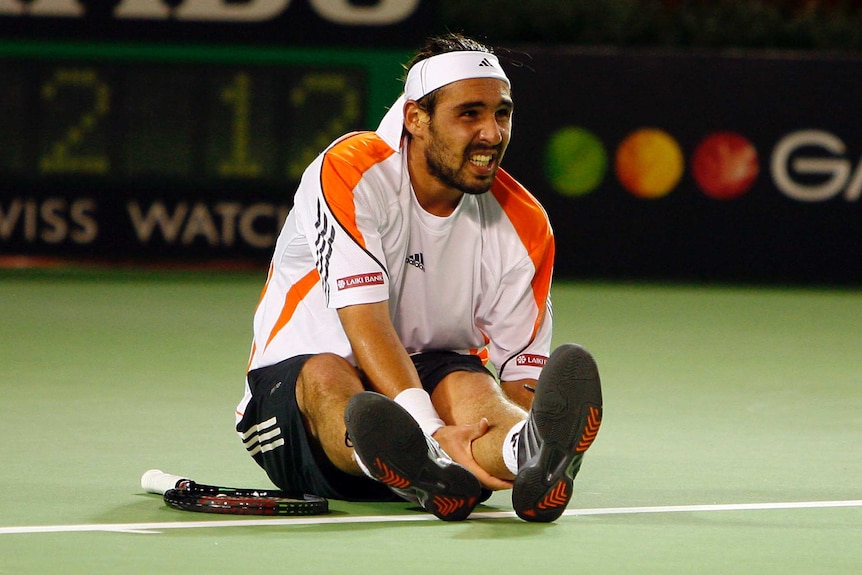 Marcos Baghdatis grimaces and holds his calf while sitting on the court during the Australian Open final.
