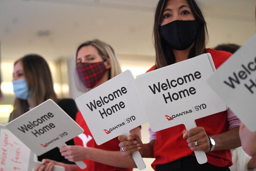 Qantas staff stand with 'welcome home' paddles
