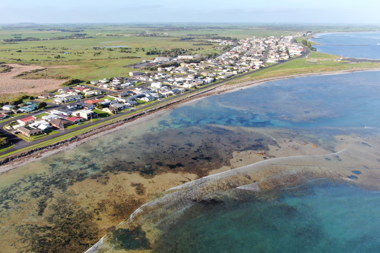 A drone shot of the coastline with houses and sand build up in the water.