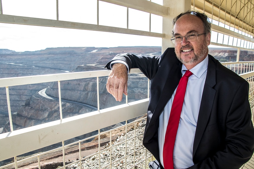 Man in suit standing at a public lookout overlooking a large gold mine
