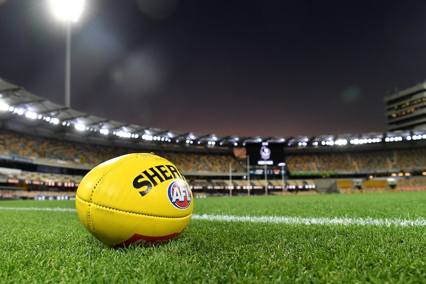 A yellow AFL ball sits on the boundary ahead of a night game at the Gabba.