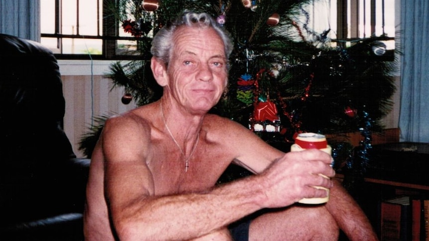 Barry sitting in front of a Christmas tree with a drink.
