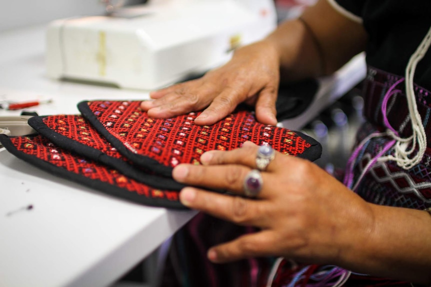 A Karen woman displays her handiwork, oven mitts made of traditional Karen design.