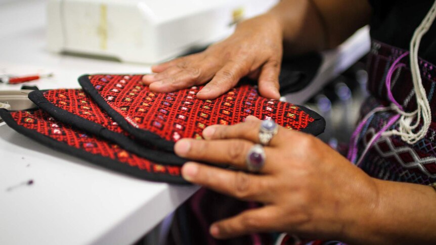 A Karen woman displays her handiwork, oven mitts made of traditional Karen design.