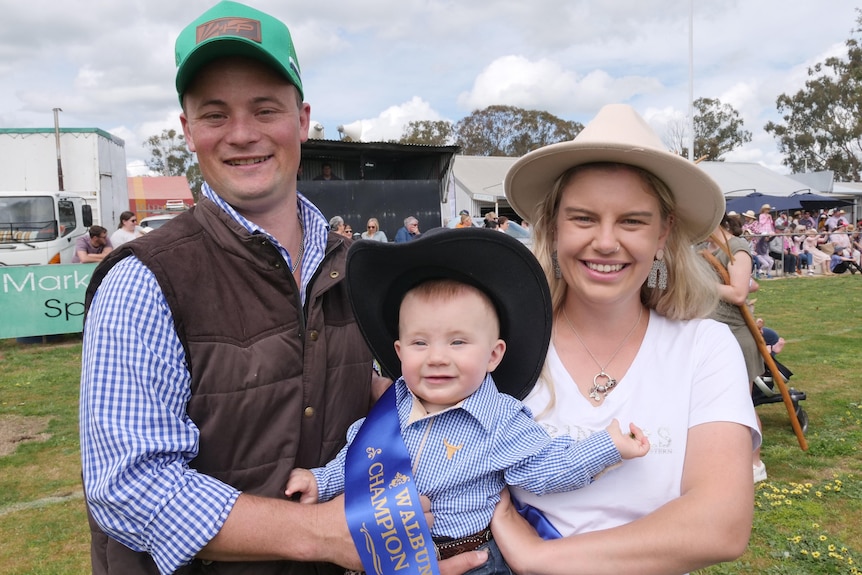 A man and woman holding their baby son who has a winner's sash around his body 