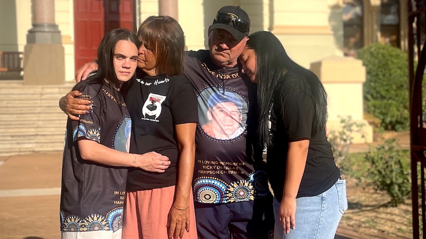 A man and a woman are supported and hugged by their daughters.