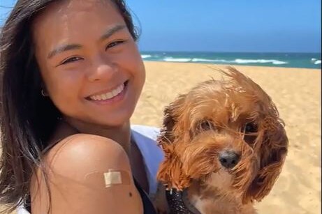 a woman holding a dog standing on a beach showing off her arm with a bandaid