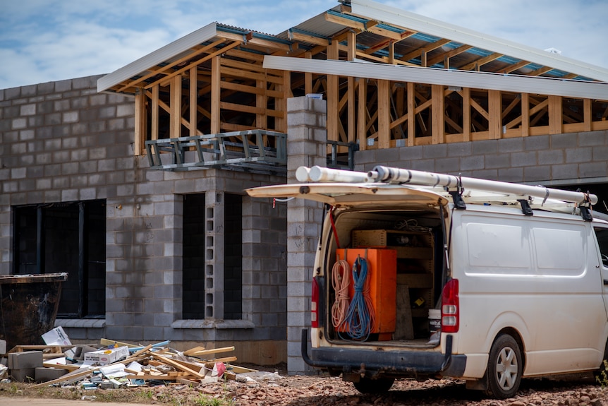 Construction site of a grey house that's almost finished with a tradie's van parked at the front on a sunny blue sky day. 