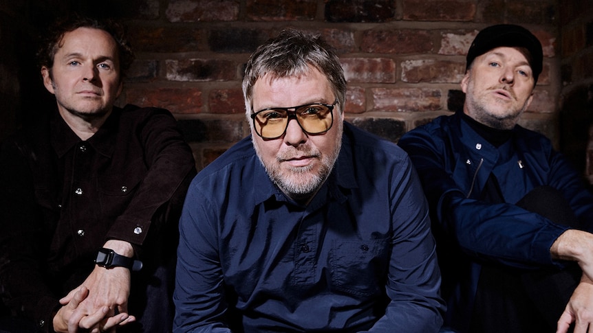 Three members of UK band Doves sit in front of a brick wall