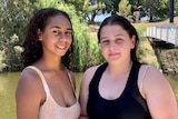 Two teenagers stand on the banks of a river in their swimmers.