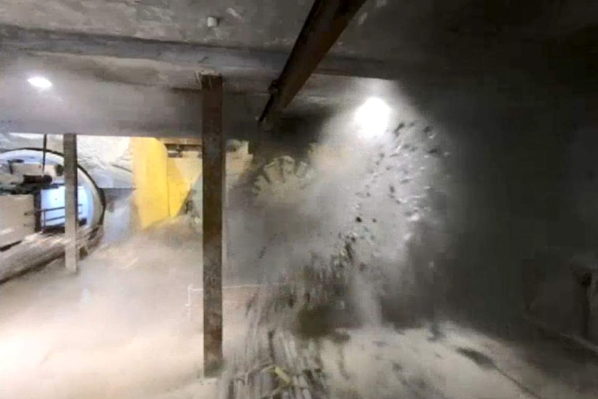A big machine breaks through a concrete wall causing dust and water to splash everywhere.