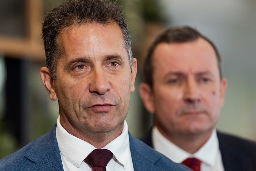 A headshot of Paul Papalia in a blue suit with Mark McGowan in the background.
