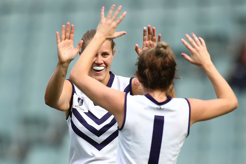 Two women's Fremantle Dockers players celebrate by exchanging  a high ten.