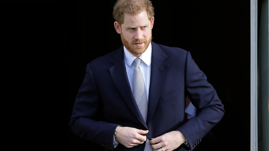 A man looks to his left as he buttons his suit jacket