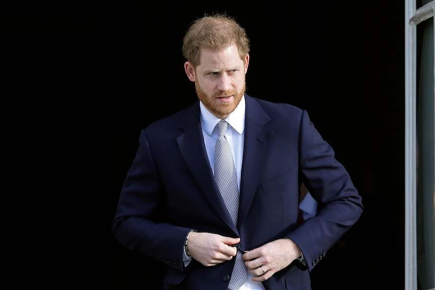 A man looks to his left as he buttons his suit jacket