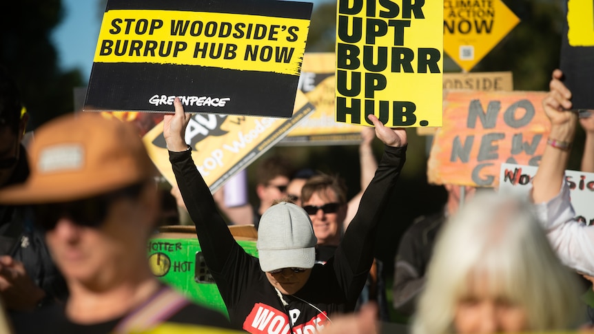 Protesters holding signs protesting against Woodside's Burrup Hub development.
