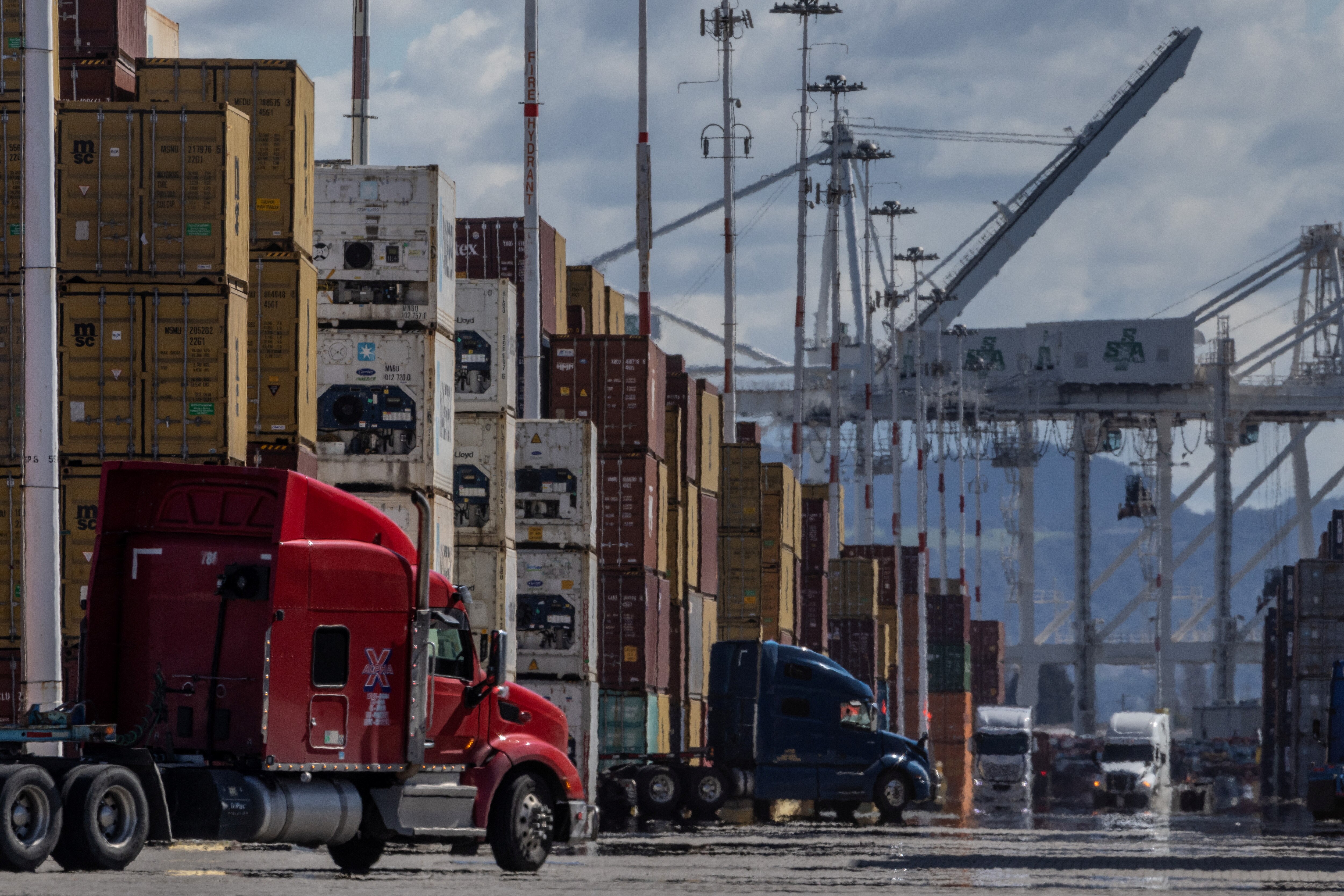 Rows of trucks are parked next to several shipping containers stacked on top of the other.