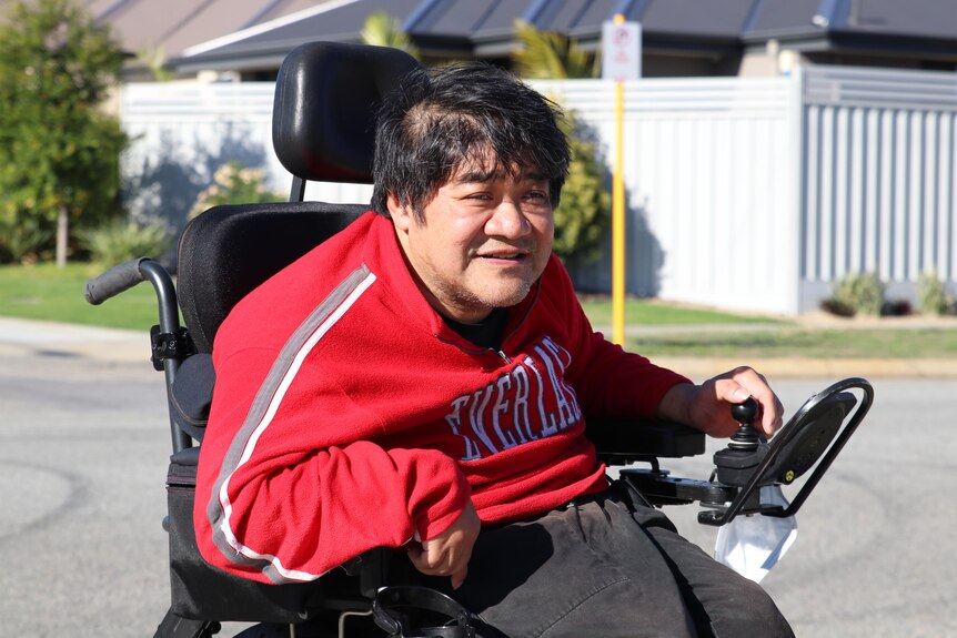 Roland wears a bright red jumper pictured outside in a wheelchair