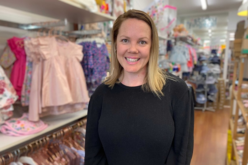 A woman stands in a store with children's clothes behind her.