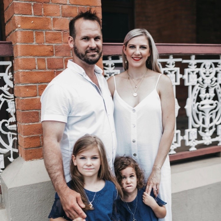 Anthony Gabiola in white shirt and Jessie Pegoraro in white dress posing for a photo with their daughters wearing blue dresses