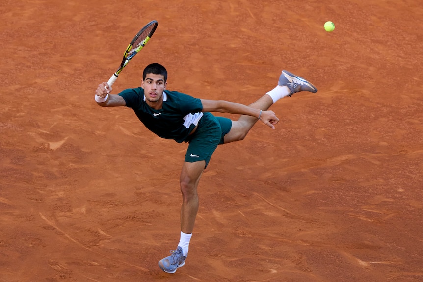 Carlos Alcaraz stretches to return a ball on a clay court.