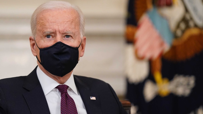 An old man in a suit wears a face mask as he looks off camera.