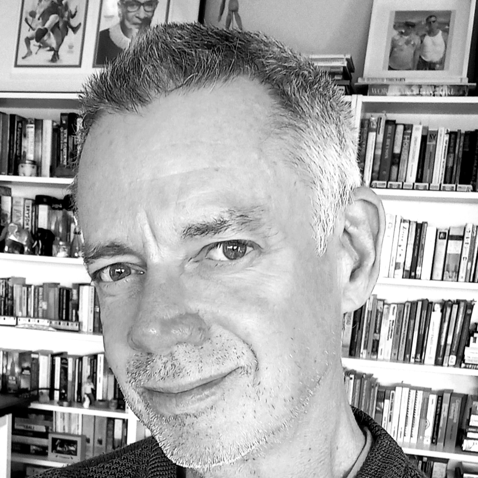 A black and white headshot of a man in front of a book shelf. 