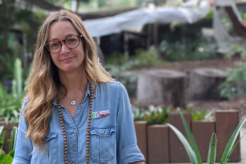 A woman in a denim dress stands outside.