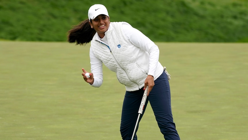 A smiling female golfer leans after picking her ball out of the cup at the US Women's Open.