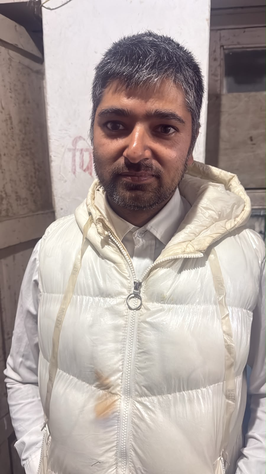 A forlorn man looks to the camera in a white jacket.